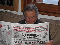 Lector consultando un ejemplar impreso del periódico francés Le Canard enchaîné