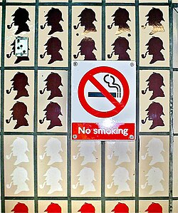 Cartel de prohibido fumar rodeado de imágenes de Sherlock Holmes fumando en una estación.