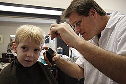 Peluquero cortándole el pelo a un niño en un establecimiento