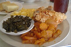 Una cena típica de soul food que incluye pan de maíz, col rizada, macarrones con queso, pollo frito, ñame y té dulce.