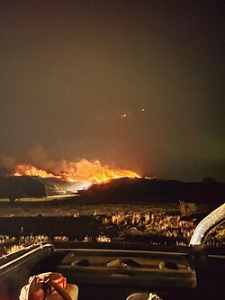 Incendio forestal avanzando con llamas visibles sobre terreno serrano.