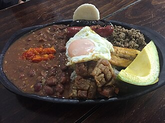 Fotografía y presentación en plato de una bandeja paisa tradicional con sus diversos componentes.
