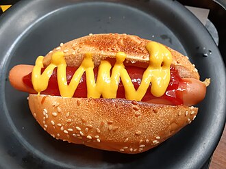 Un hot dog con kétchup y mostaza, aderezos comunes que acompañan a los hot dogs.