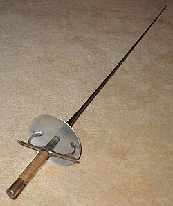 Florete equipado con una empuñadura italiana clásica en una competición o sala de armas.