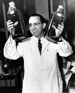 Jonas Salk sosteniendo botellas de cultivo para la vacuna contra la poliomielitis.