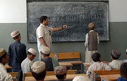 Un maestro afgano señala una pizarra explicativa frente a sus alumnos.