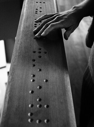 Mano leyendo código braille tallado en madera con la palabra premier
