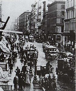 Vista de la calle Broadway en el año 1860 con carruajes tirados por caballos y edificios de la época.