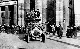 Soldados revolucionarios con bandera roja frente a la Puerta de Brandeburgo