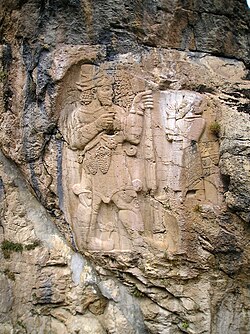 Bajorrelieve en roca que muestra a una figura ofreciendo un racimo de uvas.