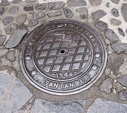 Tapa de registro de alcantarillado en Potes con alusión al organismo de reconstrucción