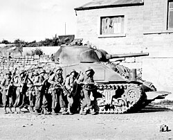 Infantería estadounidense avanzando con un carro Sherman en Bélgica