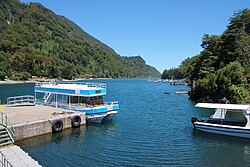 Muelle de madera en la orilla de un lago rodeado de vegetación y montañas