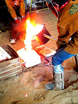 Fotografía del proceso de colado de metal fundido en un molde.