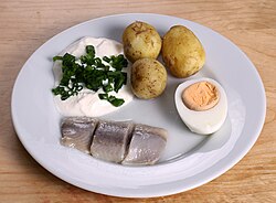 Plato de encurtido de arenque servido con crema agria, cebollines, patatas y huevo