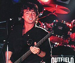 Tony Lewis tocando el bajo y cantando durante una actuación con The Outfield en 1986.