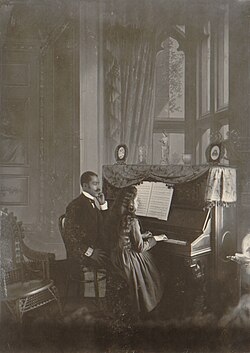 Un hombre afroestadounidense dando una lección de piano a una joven mujer blanca a finales del siglo XIX.